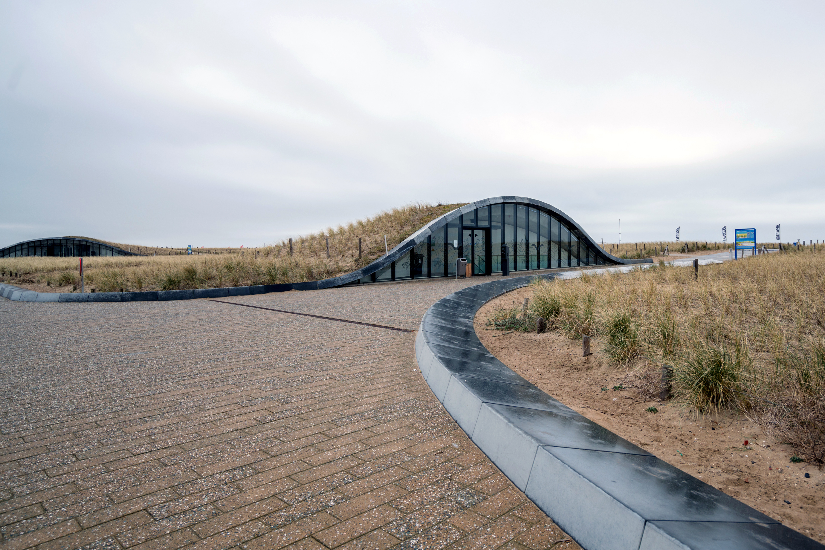 A grass-and-glass entrance to the underground parking garage built alongside the protective barrier.