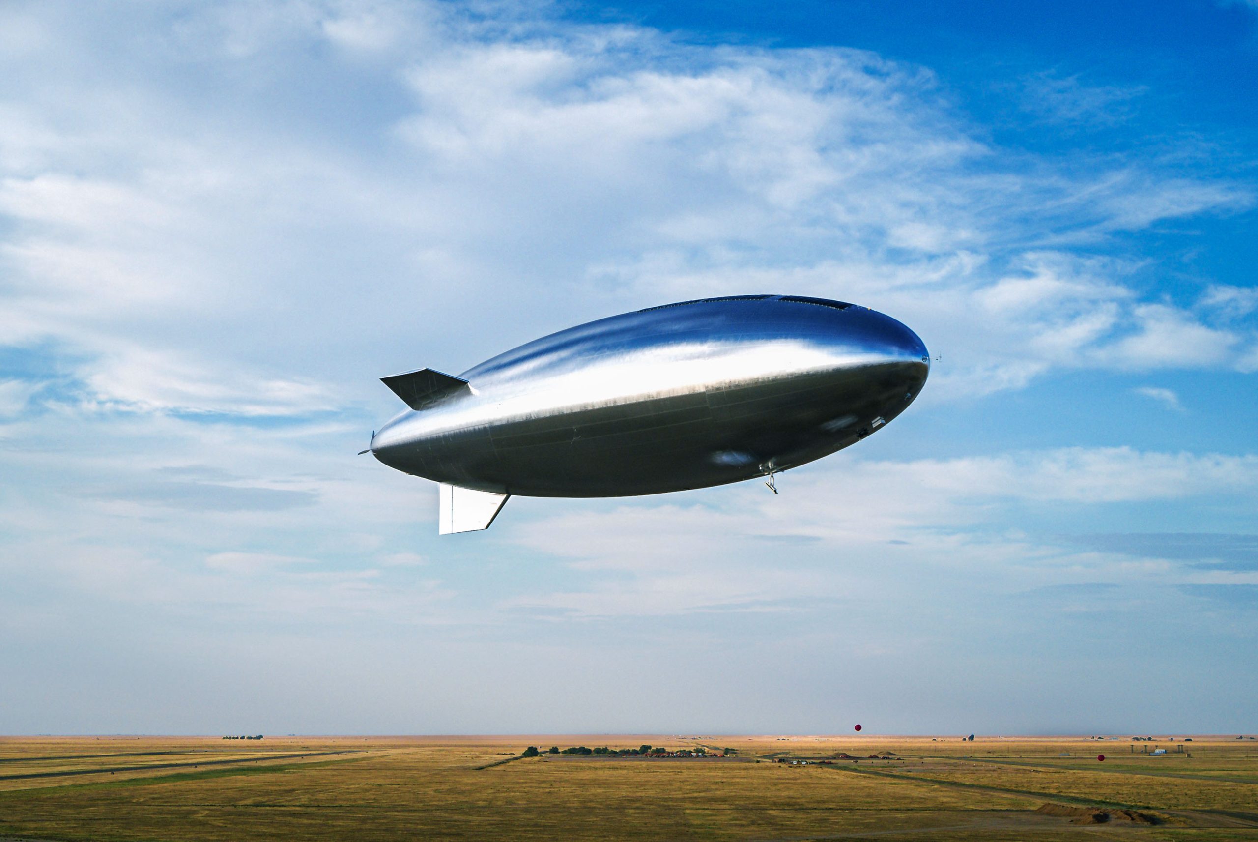 a silver blimp-like aircraft hovering over a field
